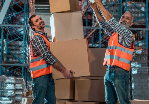 smiling-warehouse-workers-holding-stacked-boxes-an-2023-11-27-05-18-45-utc.jpg